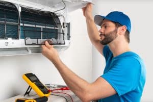 Installation service fix repair maintenance of an air conditioner indoor unit, by cryogenist technican worker checking the air filter in blue shirt and baseball cap